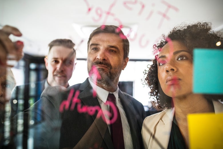 Two white men and one black woman sticking paper on glass board